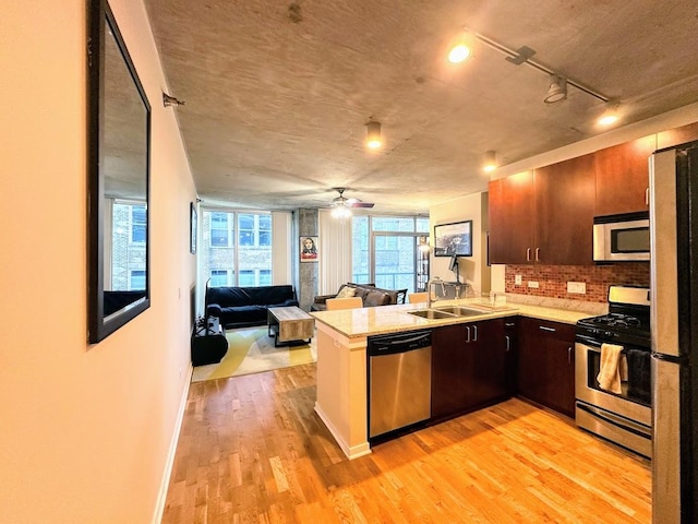 kitchen with kitchen peninsula, light hardwood / wood-style flooring, appliances with stainless steel finishes, sink, and backsplash