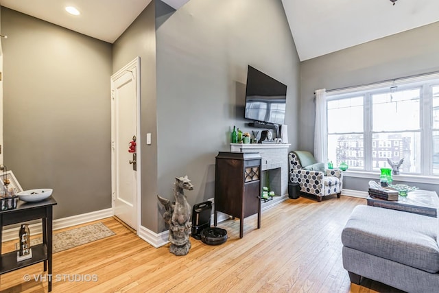 living room featuring a brick fireplace, light hardwood / wood-style flooring, and vaulted ceiling