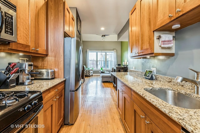 kitchen with appliances with stainless steel finishes, tasteful backsplash, sink, light stone countertops, and light wood-type flooring