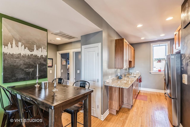 kitchen with sink, stainless steel fridge, light stone countertops, and light hardwood / wood-style floors