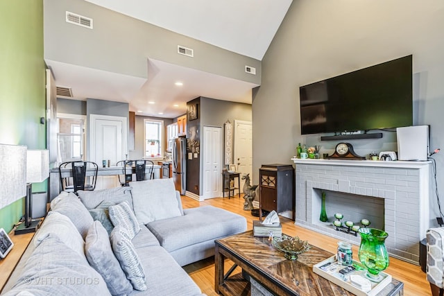 living room with high vaulted ceiling, a fireplace, and light hardwood / wood-style floors