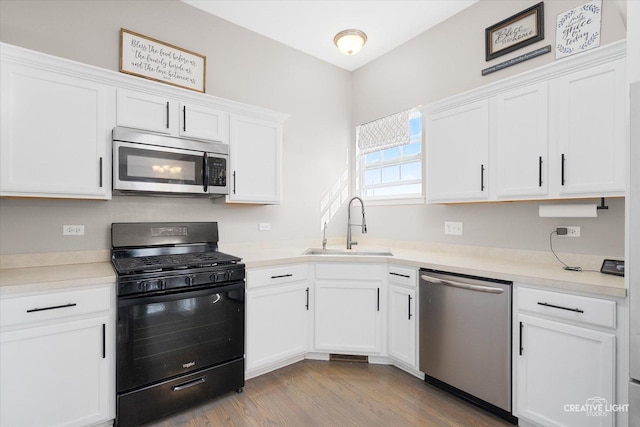 kitchen featuring appliances with stainless steel finishes, sink, white cabinets, and light wood-type flooring