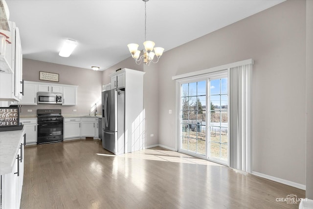 kitchen featuring wood-type flooring, decorative light fixtures, stainless steel appliances, light stone countertops, and white cabinets