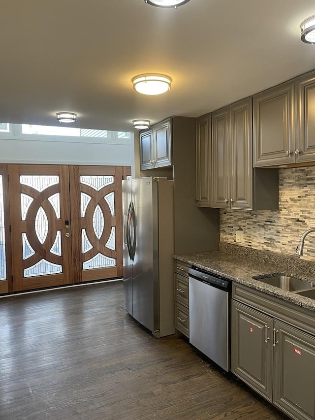 kitchen featuring appliances with stainless steel finishes, sink, dark wood-type flooring, dark stone counters, and decorative backsplash