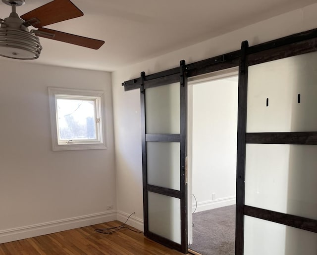 empty room featuring ceiling fan, hardwood / wood-style floors, and a barn door