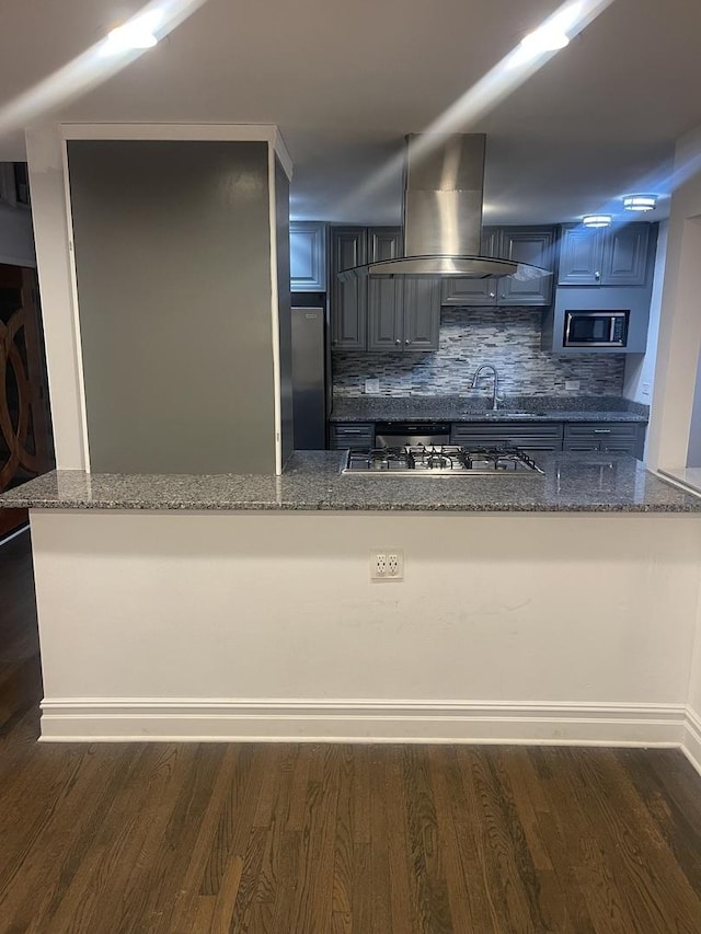 kitchen featuring dark stone counters, kitchen peninsula, appliances with stainless steel finishes, and island range hood