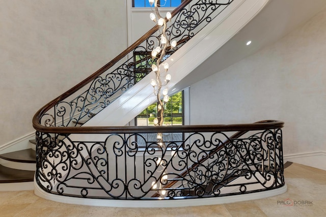 stairway with a towering ceiling, plenty of natural light, and a notable chandelier