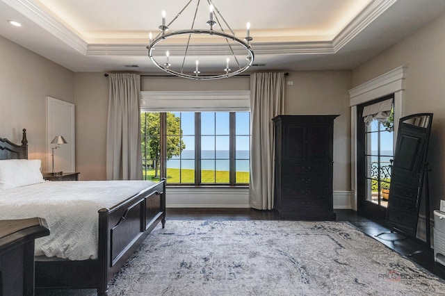 bedroom with a water view, dark hardwood / wood-style floors, a raised ceiling, and a chandelier