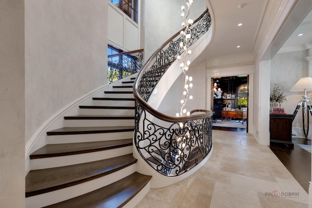 stairs featuring ornamental molding, a towering ceiling, and a chandelier