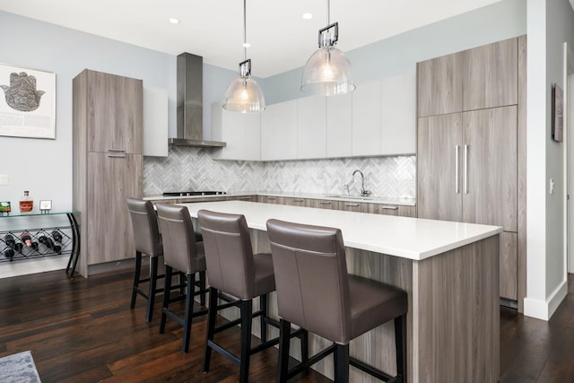 kitchen featuring dark hardwood / wood-style flooring, a kitchen island, wall chimney exhaust hood, white cabinets, and sink