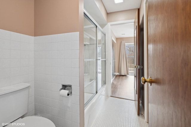 bathroom featuring tile walls, tile patterned floors, shower / bath combination with glass door, and toilet