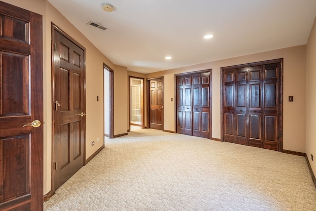 unfurnished bedroom with multiple closets and light carpet