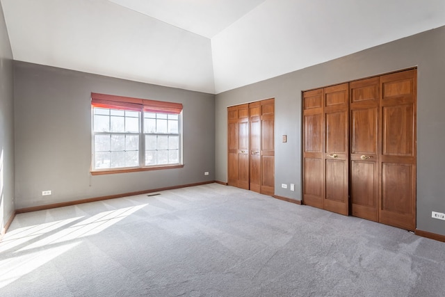 unfurnished bedroom featuring multiple closets, light colored carpet, and lofted ceiling