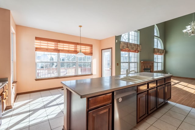 kitchen featuring light tile patterned floors, hanging light fixtures, a wealth of natural light, a center island with sink, and stainless steel dishwasher