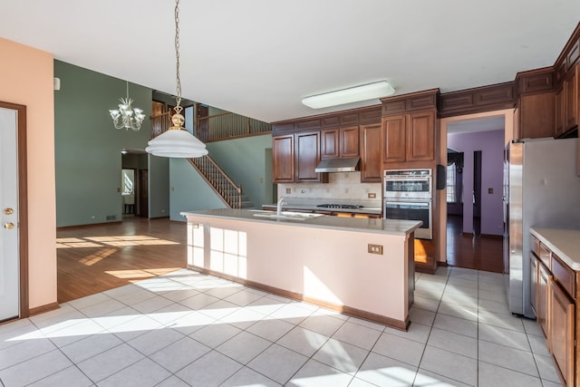 kitchen featuring sink, light tile patterned floors, appliances with stainless steel finishes, hanging light fixtures, and an island with sink