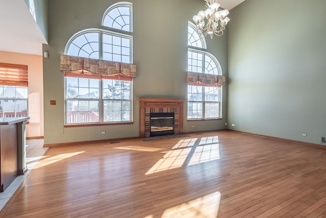 unfurnished living room with a high ceiling, a brick fireplace, a chandelier, and light hardwood / wood-style floors