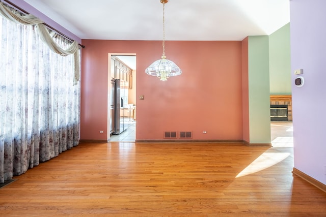 unfurnished dining area featuring a fireplace, light hardwood / wood-style floors, and a chandelier