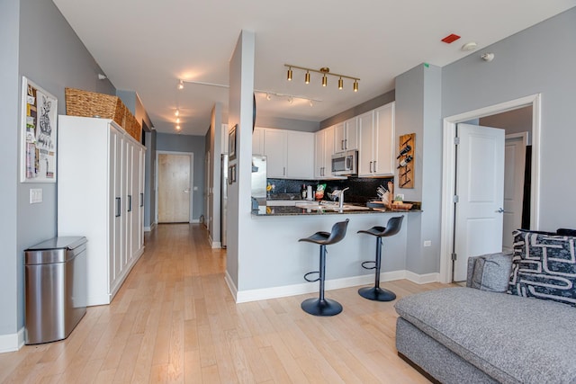 kitchen with white cabinetry, a kitchen bar, kitchen peninsula, backsplash, and light hardwood / wood-style flooring