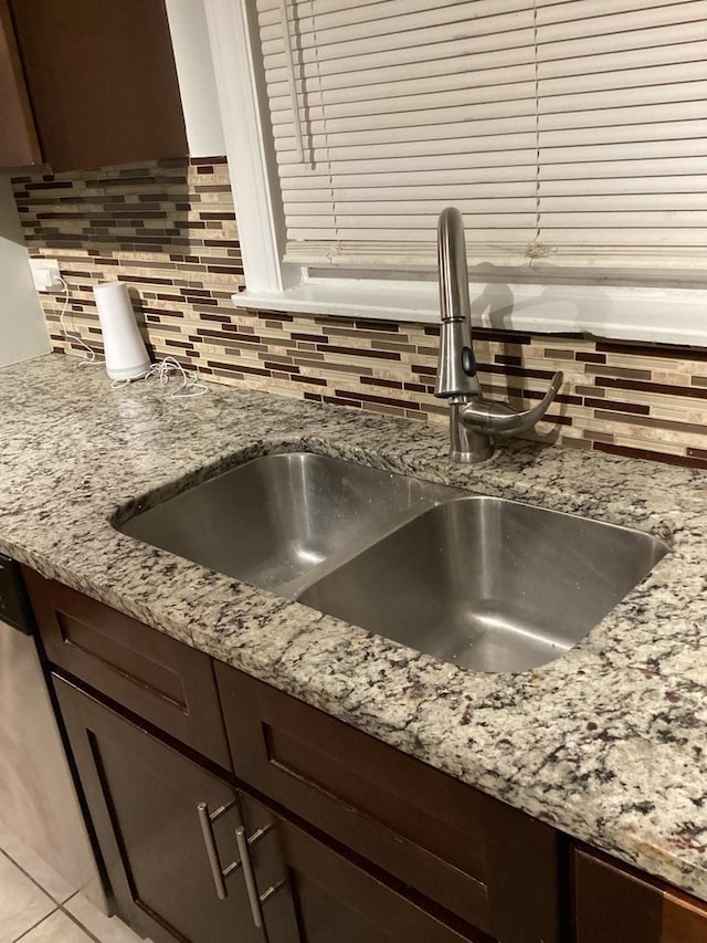 interior details featuring tasteful backsplash, dark brown cabinets, sink, and light stone counters