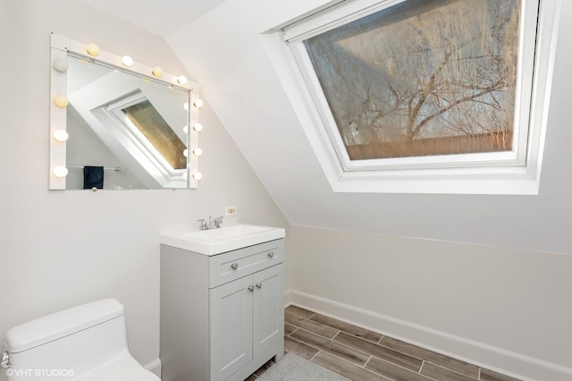 bathroom with lofted ceiling with skylight, vanity, toilet, and wood tiled floor