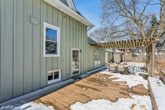 snow covered deck featuring outdoor dining area, fence, and a pergola