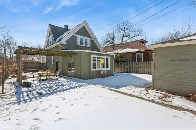 snow covered rear of property with board and batten siding, an outbuilding, fence, and a pergola