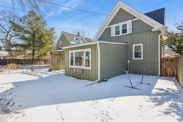 snow covered rear of property with board and batten siding and fence