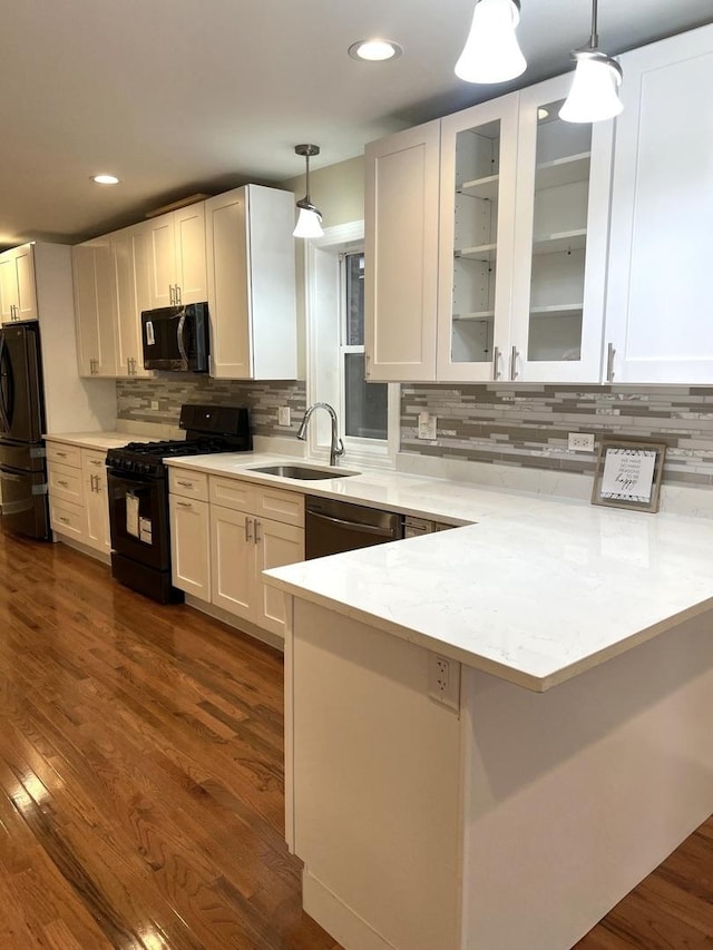 kitchen featuring decorative light fixtures, black appliances, kitchen peninsula, sink, and white cabinetry