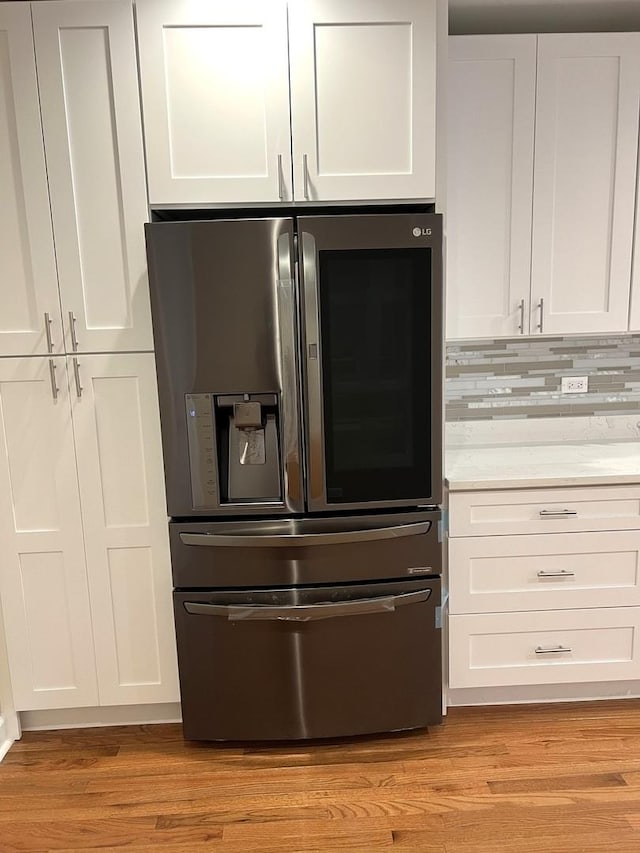 kitchen with stainless steel refrigerator with ice dispenser, white cabinetry, backsplash, and light hardwood / wood-style flooring