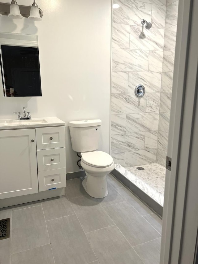 bathroom with toilet, a tile shower, tile patterned floors, and vanity