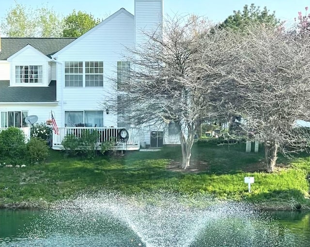 rear view of property with a deck with water view and a lawn