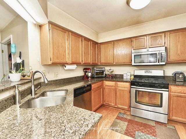 kitchen with sink, light hardwood / wood-style flooring, light stone countertops, and appliances with stainless steel finishes