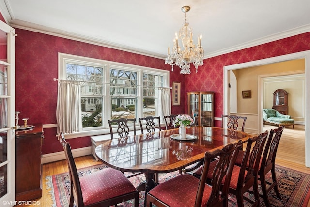 dining space featuring a notable chandelier, wood finished floors, baseboards, wallpapered walls, and crown molding