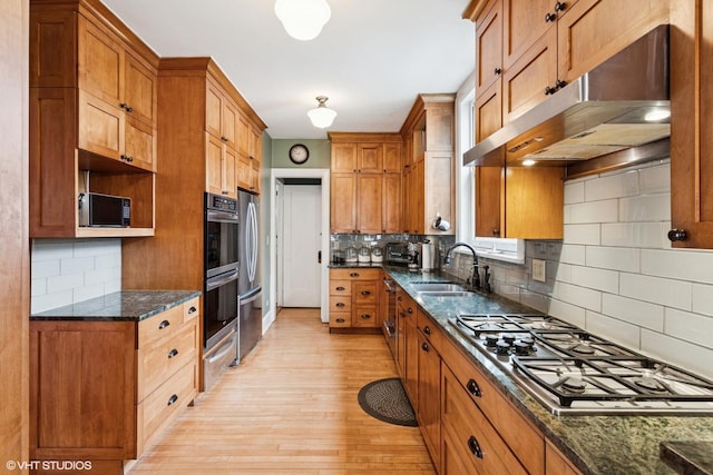 kitchen with a sink, appliances with stainless steel finishes, brown cabinets, and under cabinet range hood