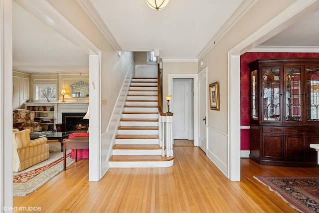 foyer with crown molding, a lit fireplace, hardwood / wood-style floors, and stairs