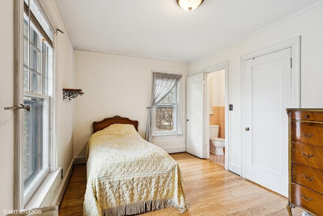 bedroom with ornamental molding, light wood finished floors, and ensuite bath