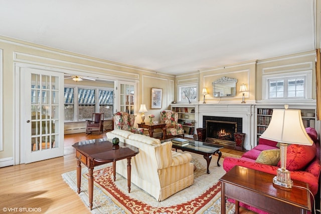 living area with crown molding, a baseboard heating unit, a brick fireplace, ceiling fan, and wood finished floors