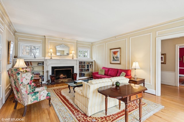 living room with a decorative wall, ornamental molding, light wood-type flooring, a warm lit fireplace, and baseboards