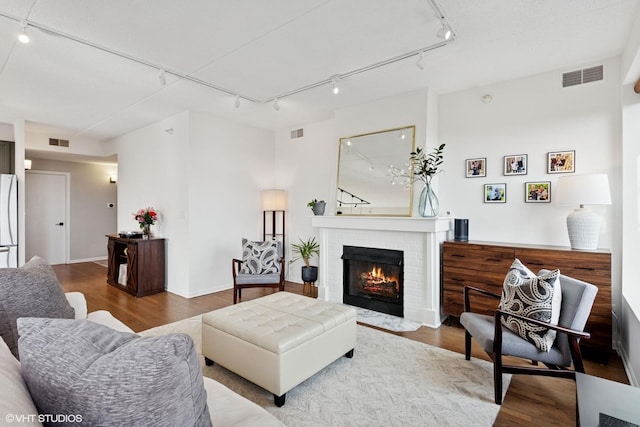 living area featuring a brick fireplace, visible vents, and wood finished floors