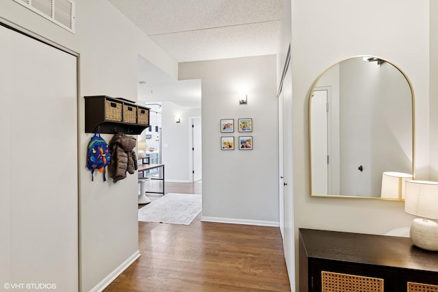 corridor with a textured ceiling, wood finished floors, visible vents, and baseboards