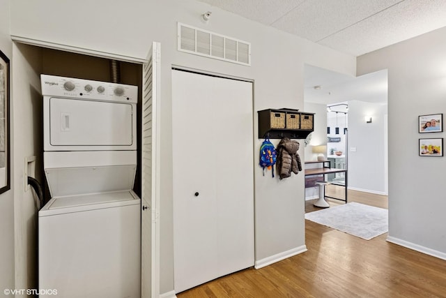 laundry area featuring laundry area, stacked washer / dryer, wood finished floors, visible vents, and baseboards