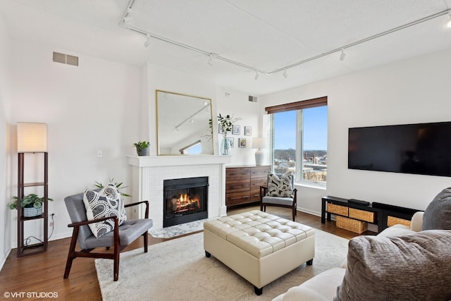 living room featuring rail lighting, a brick fireplace, visible vents, and wood finished floors