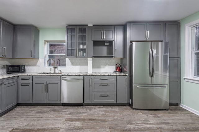 kitchen featuring light stone countertops, appliances with stainless steel finishes, light hardwood / wood-style flooring, sink, and gray cabinetry