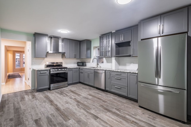 kitchen with light stone countertops, wall chimney exhaust hood, stainless steel appliances, sink, and gray cabinets