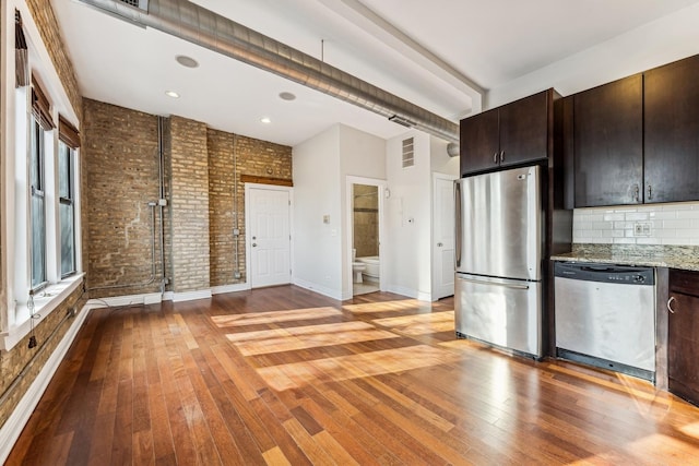 kitchen featuring dark brown cabinetry, appliances with stainless steel finishes, light stone countertops, and brick wall