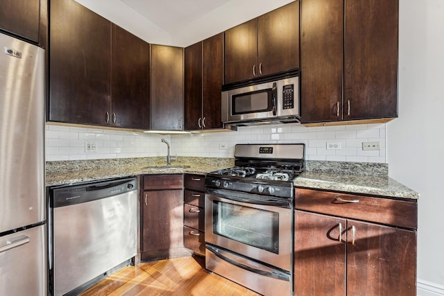 kitchen featuring sink, decorative backsplash, dark brown cabinetry, stainless steel appliances, and light stone countertops