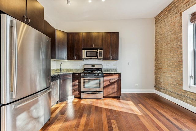 kitchen with appliances with stainless steel finishes, light stone countertops, sink, and dark brown cabinets