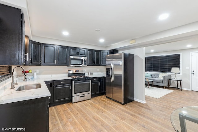 kitchen featuring sink, stainless steel appliances, light stone counters, and light hardwood / wood-style floors