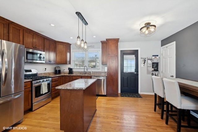 kitchen with decorative light fixtures, a kitchen island, light hardwood / wood-style flooring, appliances with stainless steel finishes, and light stone counters