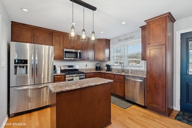 kitchen featuring light stone countertops, pendant lighting, a kitchen island, stainless steel appliances, and light hardwood / wood-style floors